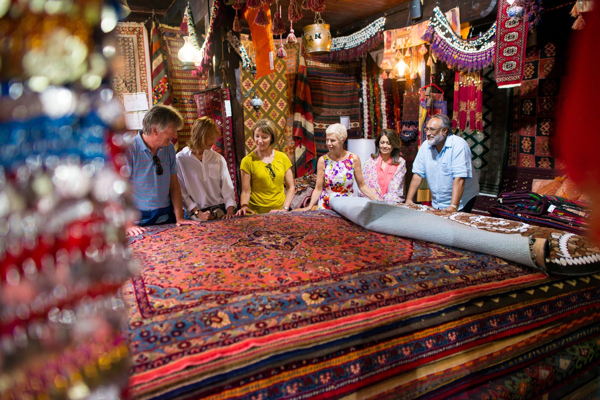 A group of people stand behind Bosnian craft carpets, in red and brown colours, in a market