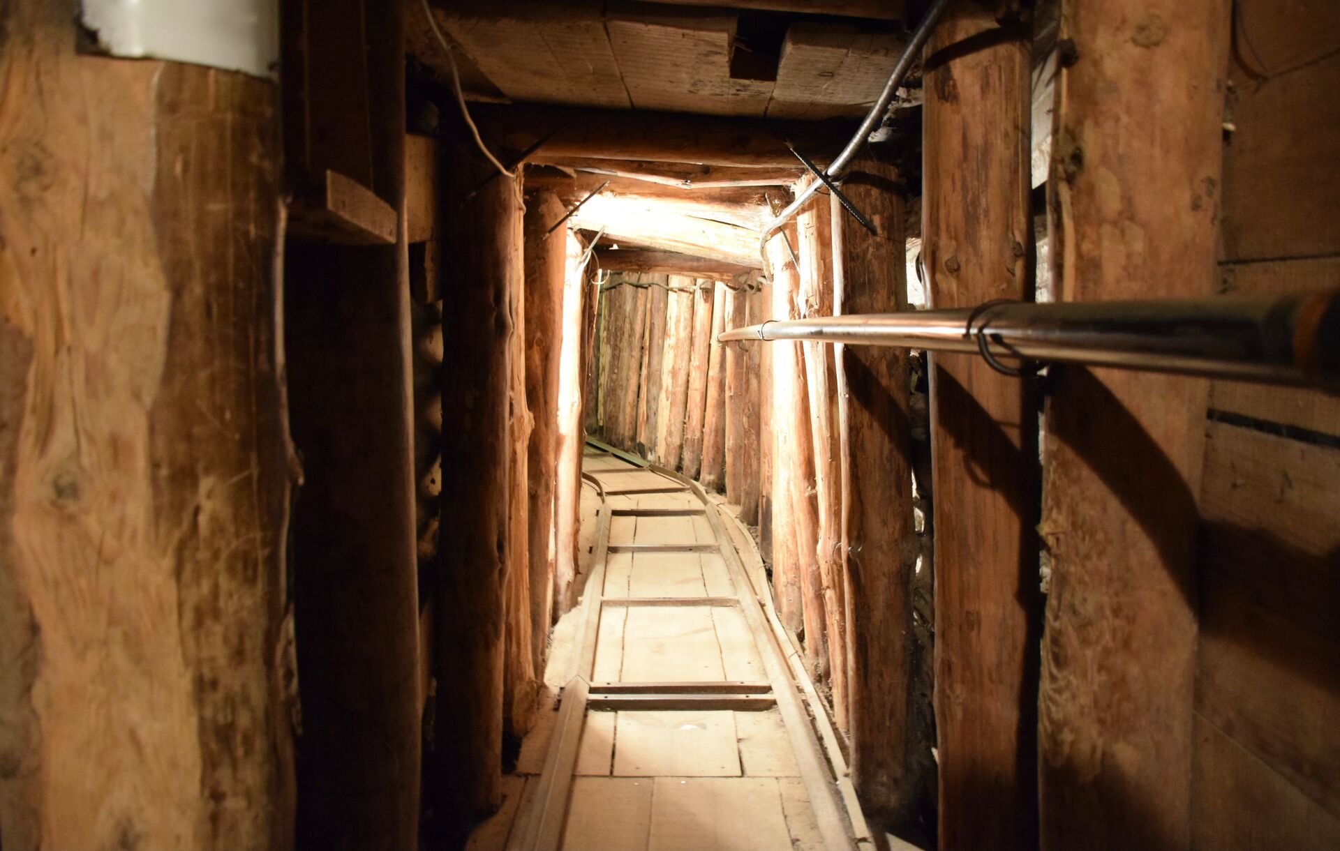 The Tunnel of Hope from the inside, showing a think tunnel and track with wooden planks on the walls and sunlight streaming through