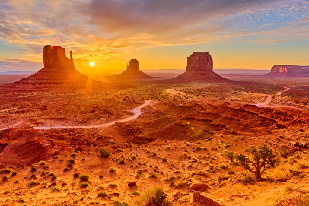 Orange sunlight bathes the red sandstone towers of Monument Valley
