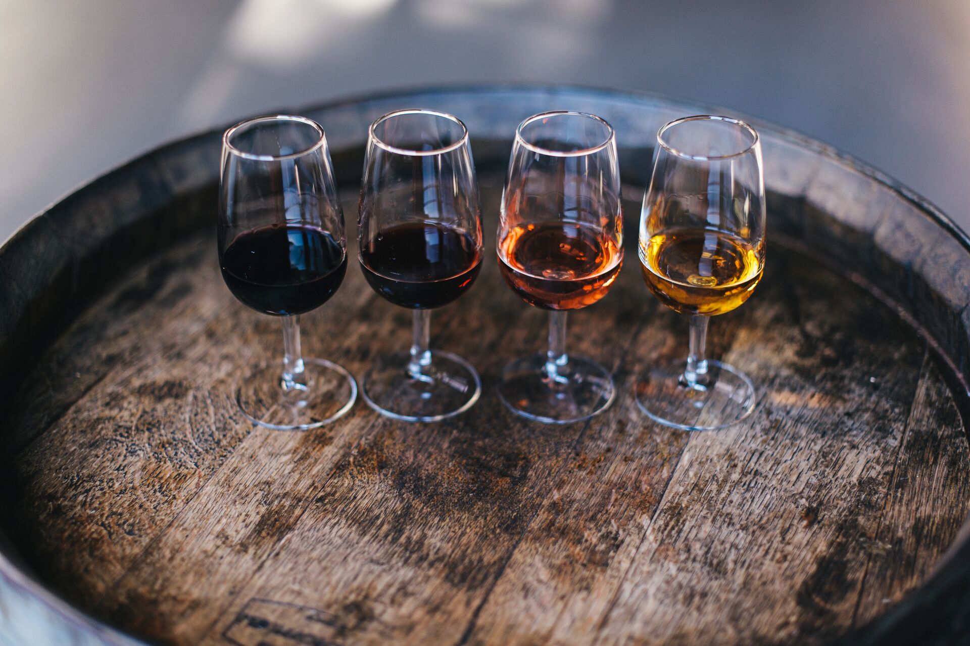 Four glasses, half full of various coloured port wine stand lined up ready for a tasting, set upon an old oak barrel.