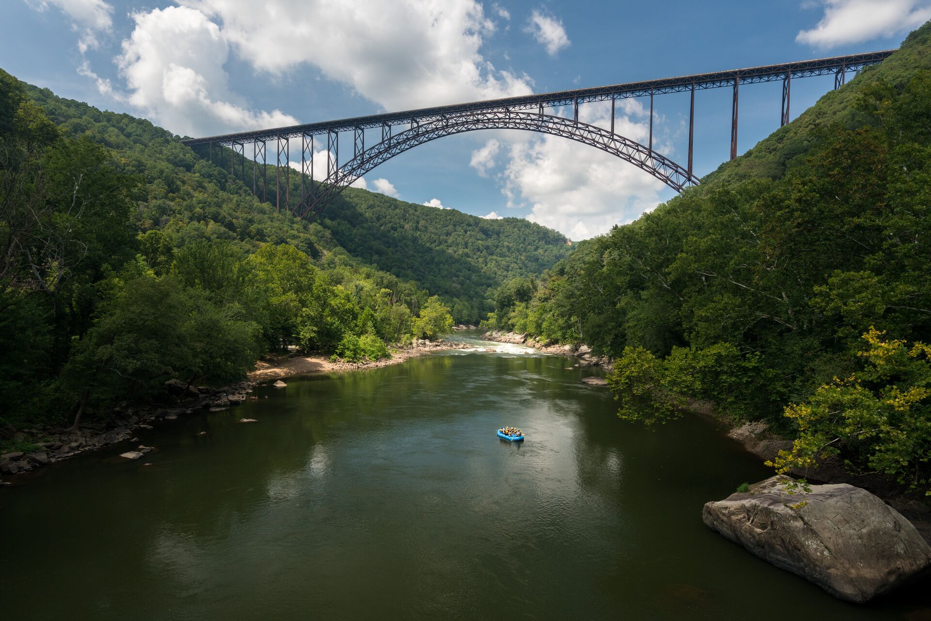 A bridge spans a deep gorge with a blue river at the bottom and green trees on either side