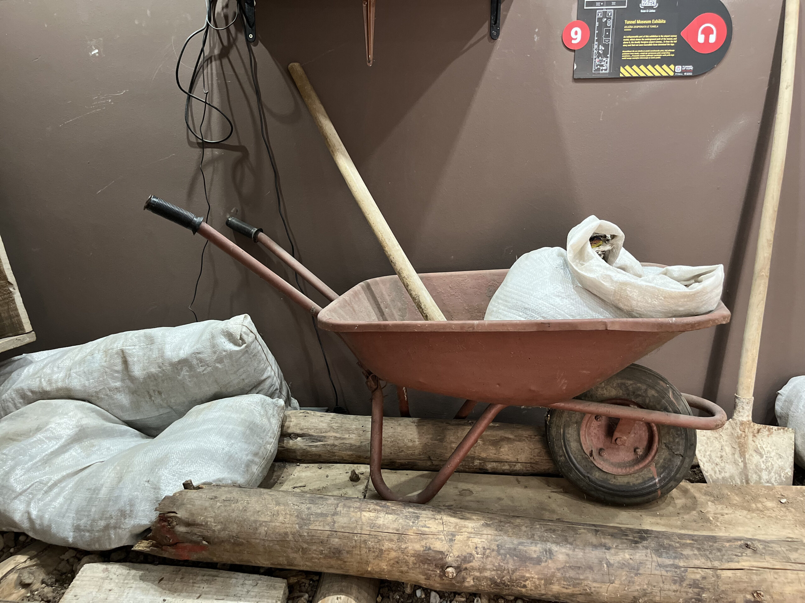 a wheelbarrow with a spade and sand bags inside is on display at the Tunnel of Hope