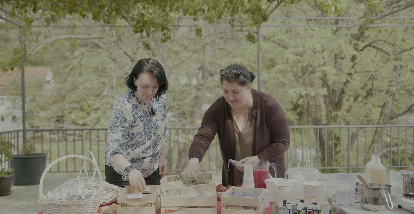 Two women stand behind a bench full of soaps on show