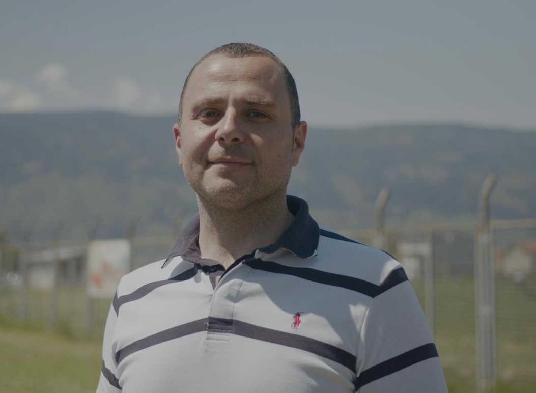 Aldin, who share his survivor’s story is pictured at the site of the Tunnel of Hope with a white and blue pol shirt with a mountain and sky in the background