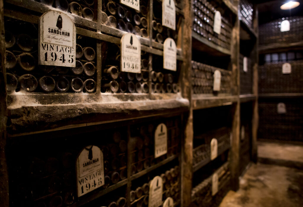 an ancient wine cellar shows stacks of bottles of Portugal’s oldest wine, Port, with white labels marking the vintage years in the 1940s