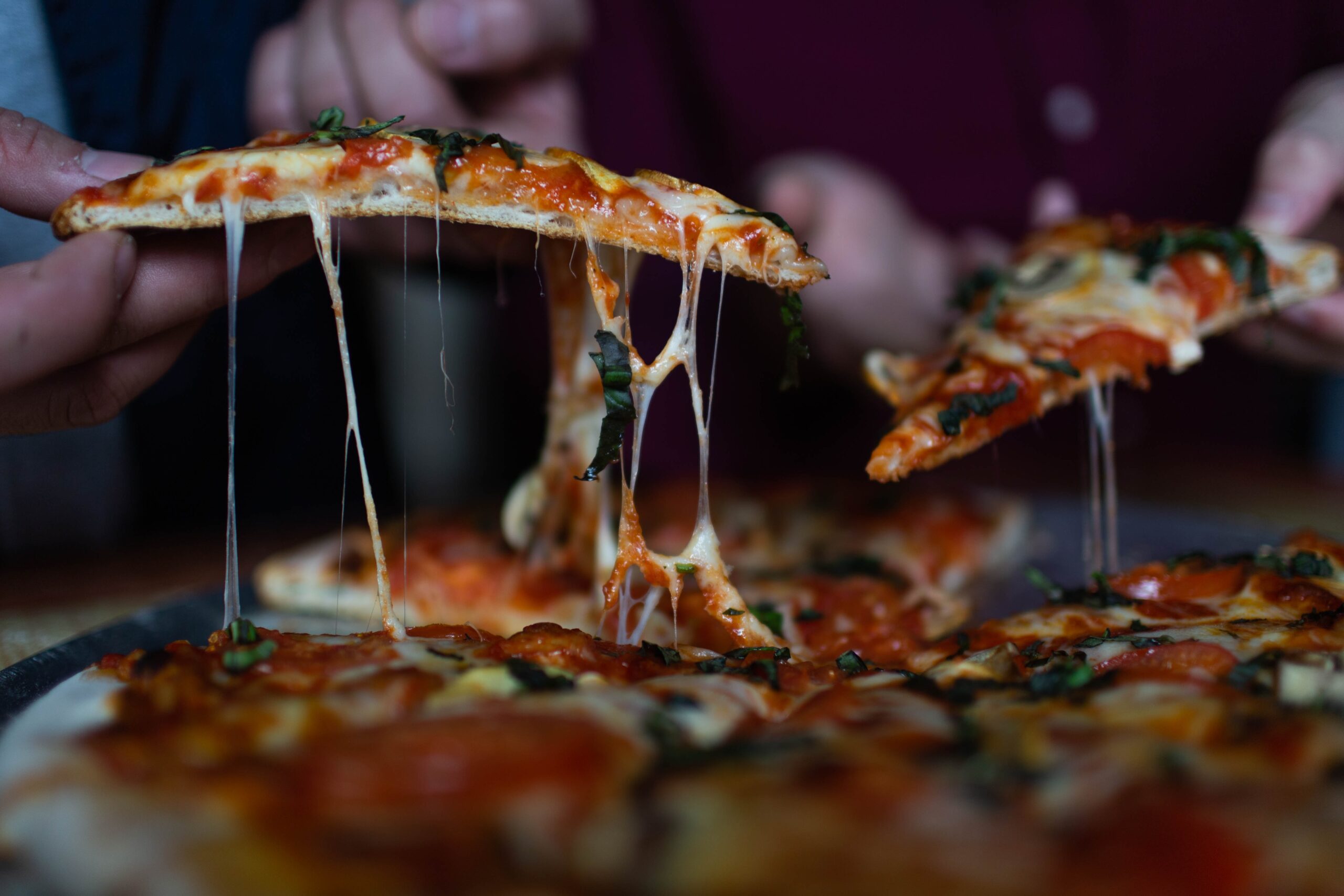 slices of pizza being picked up from a plate with cheese flowing over the edges