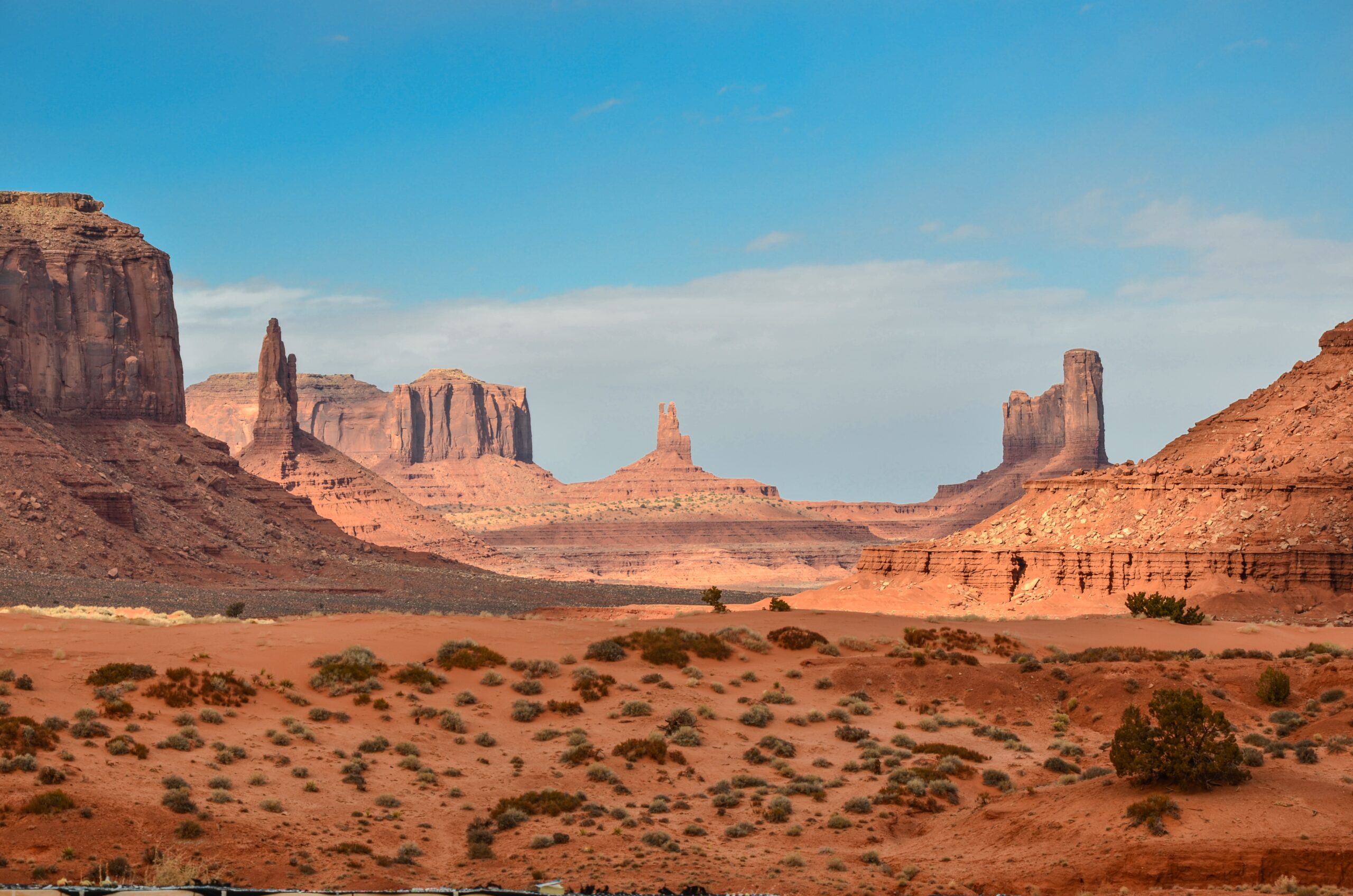 Red sandstone towers flank a red sand valley, with a bright blue sky