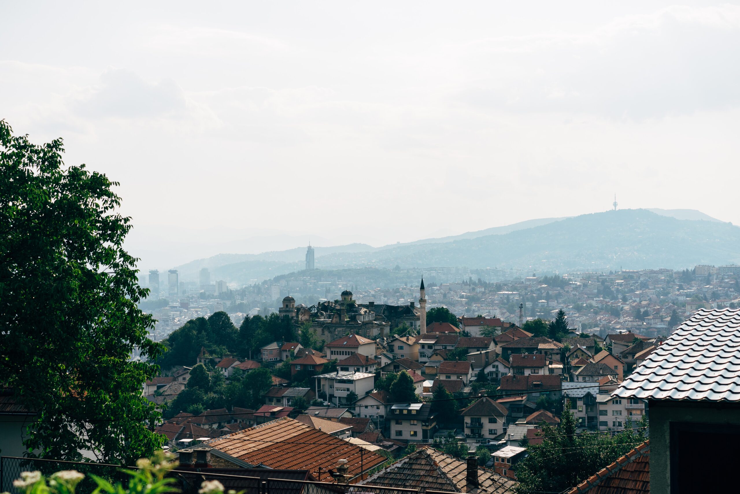 Ariel shot across the buildings of Sarajevo with a misty sky and rolling mountains in the background