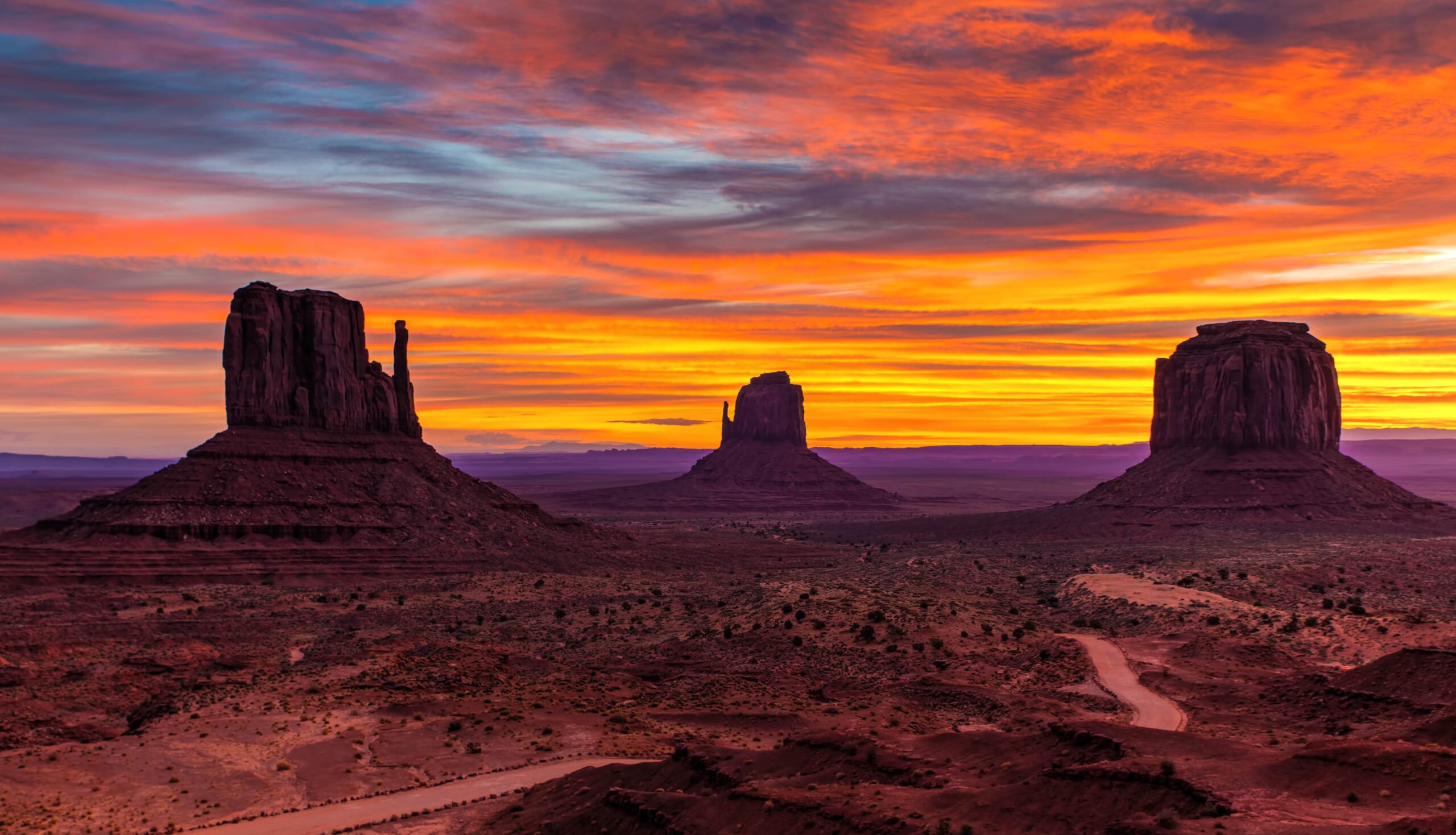 Sun sets over Monument Valley with red, gold and orange skies and dark rock towers under shadow