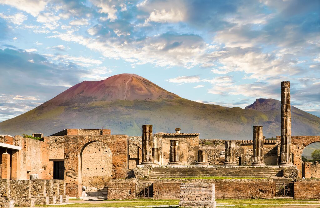 The ruins of Pompeii in the sunlight, dwarfed by Mount Vesuvius in the background