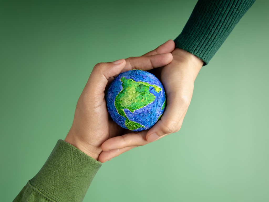 Two hands holding a small earth globe, symbolizing the environmental impacts of tourism, on a green background.