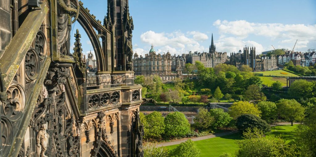 A view out over Edinburgh shows green parks and trees with an ancient building in the foreground