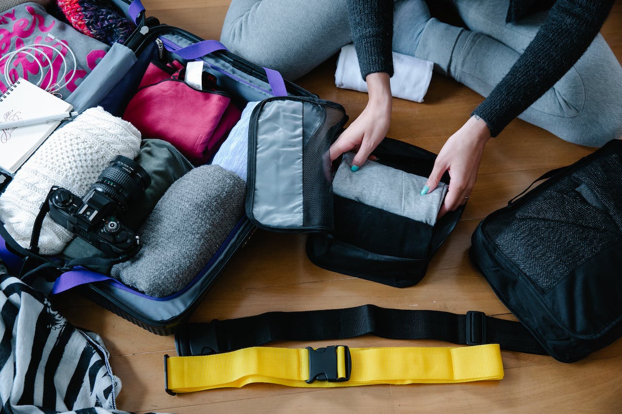 female hands packing clothes and a camera into a suitcase