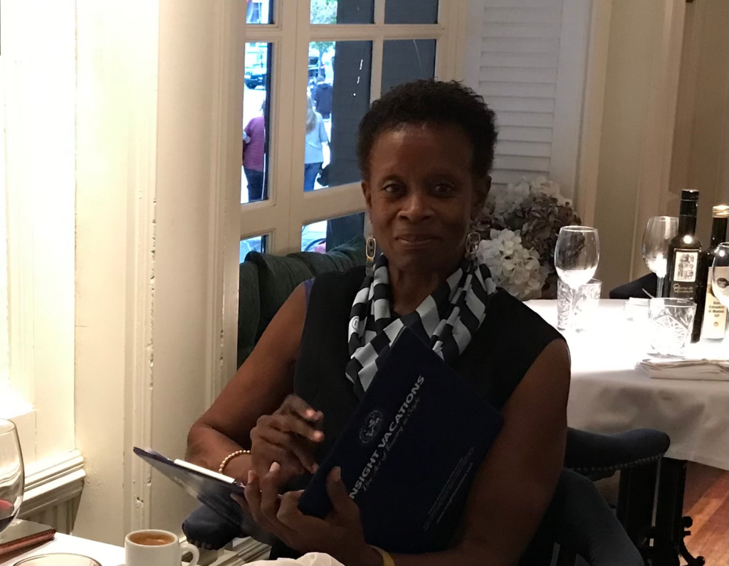 A picture of Betty, one of our global travel experts, sitting at a restaurant with an Insight Vacations booklet in her hands