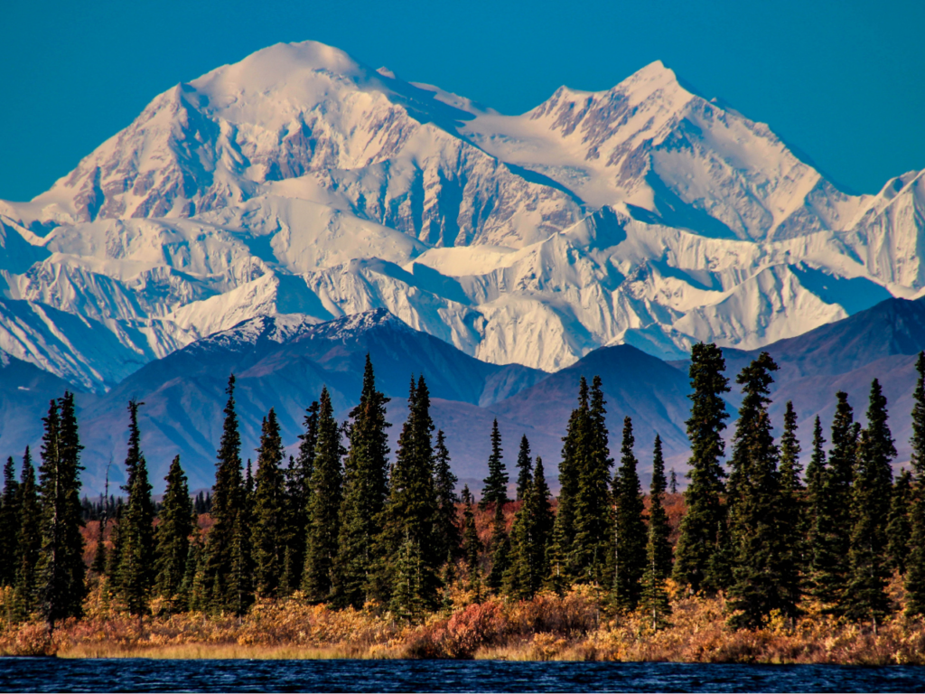 An Alaskan landscape: a river and forest in the foreground, backdropped by a colossal mountain range