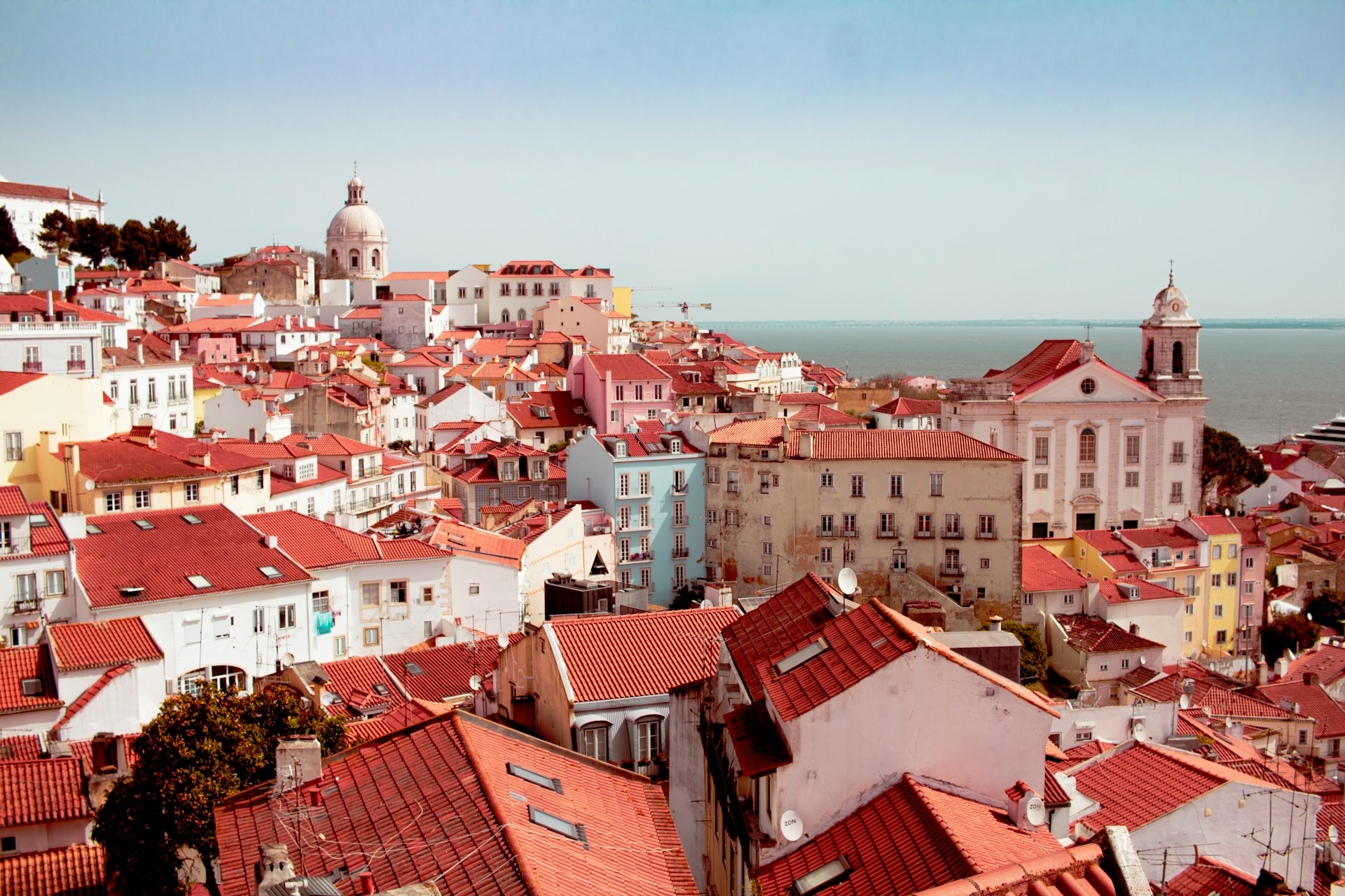 Photo of Lisbon's red-tiled rooftops, with the Atlantic Ocean visible in the distance