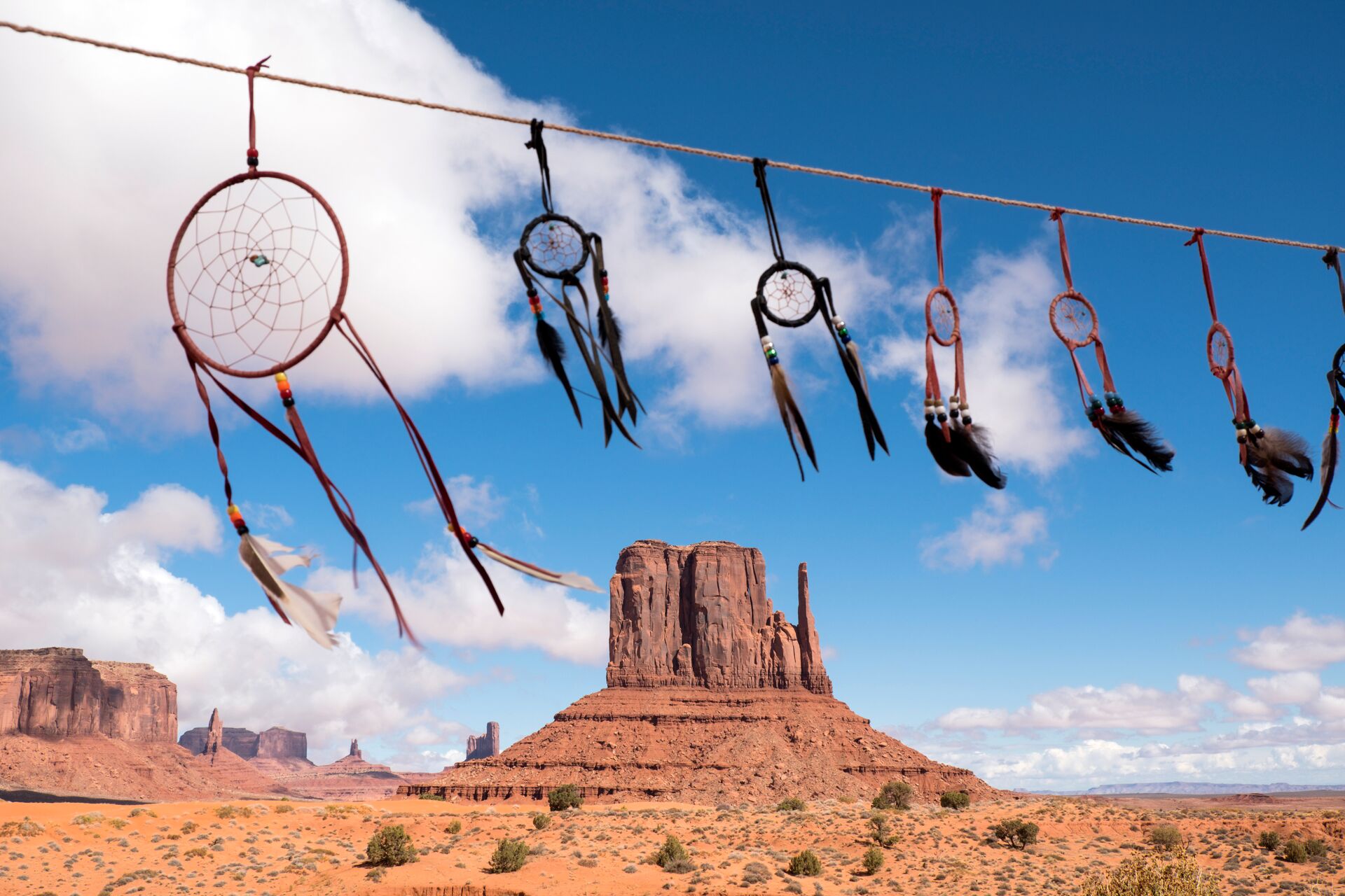Image of West Mitten Butte in Monument Valley, blue sky with clouds, in the foreground dreamcatchers hanging from a line