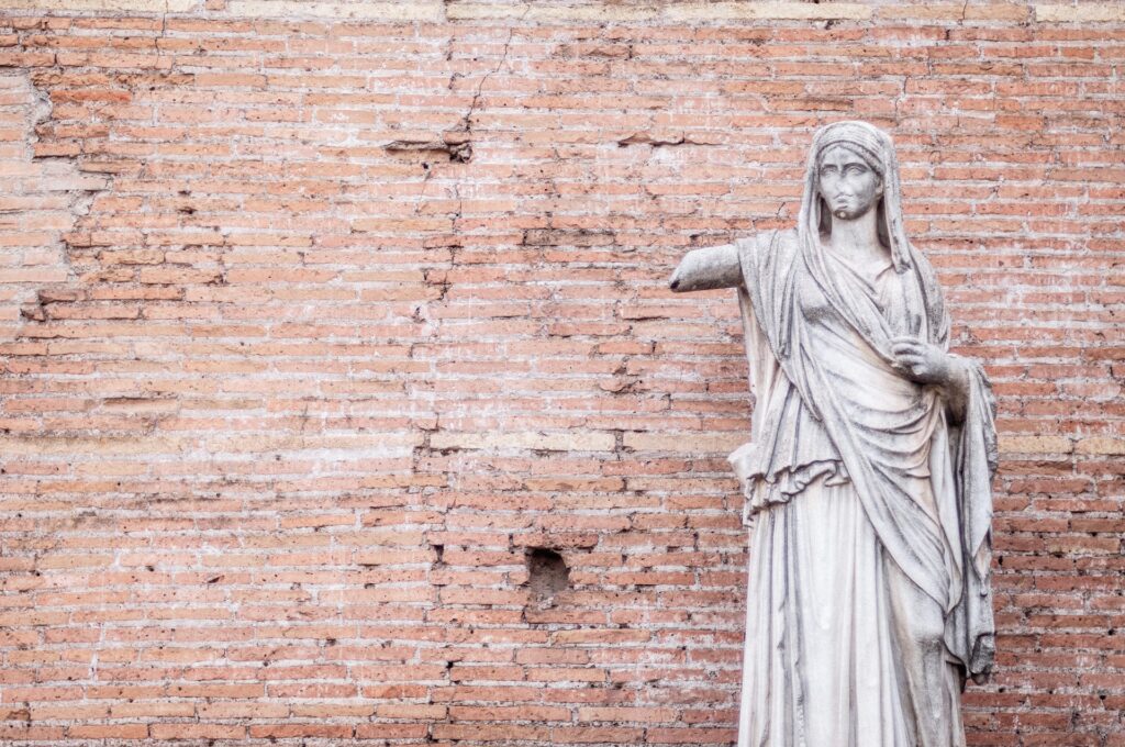 Female statue standing in front of a brick wall