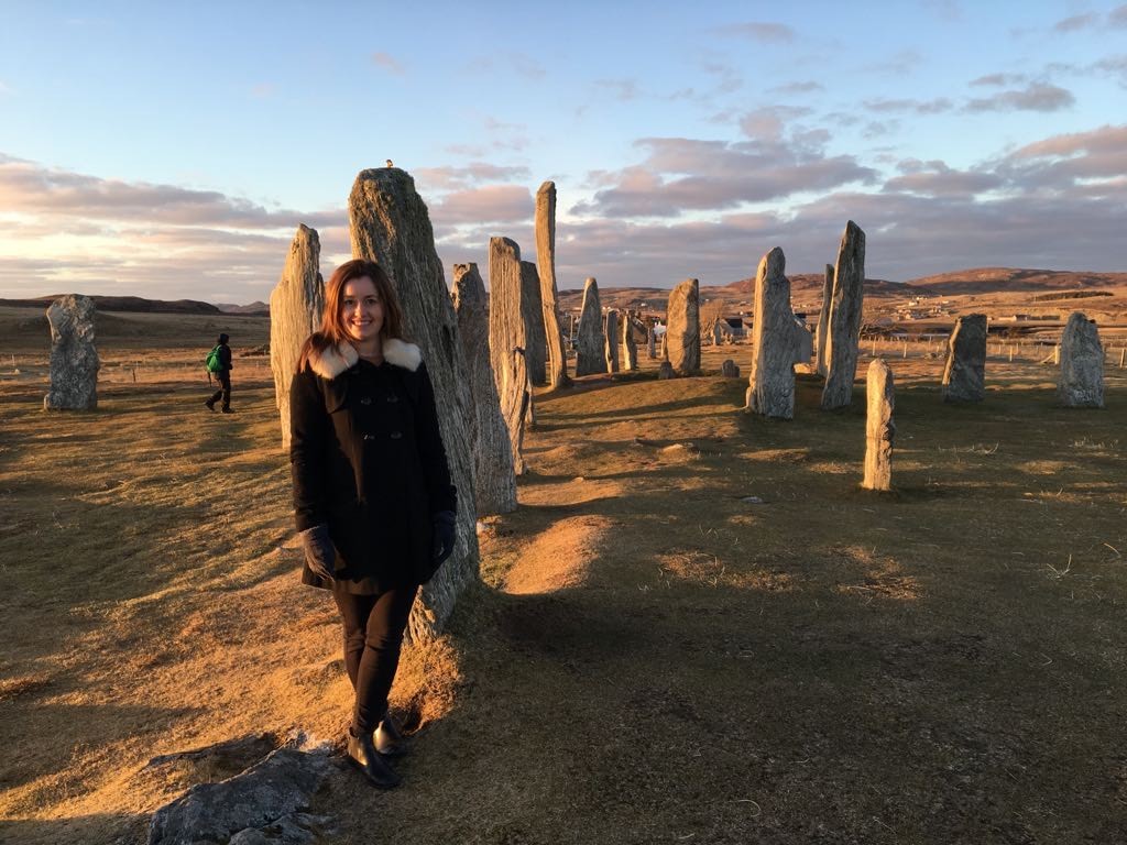 Photo of Lyn standing against the Calanais Standing Stones, at sunset against a blue sky
