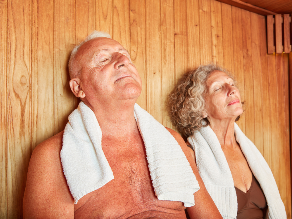 Couple enjoying a sauna session, closing their eyes with towels wrapped around their necks.
