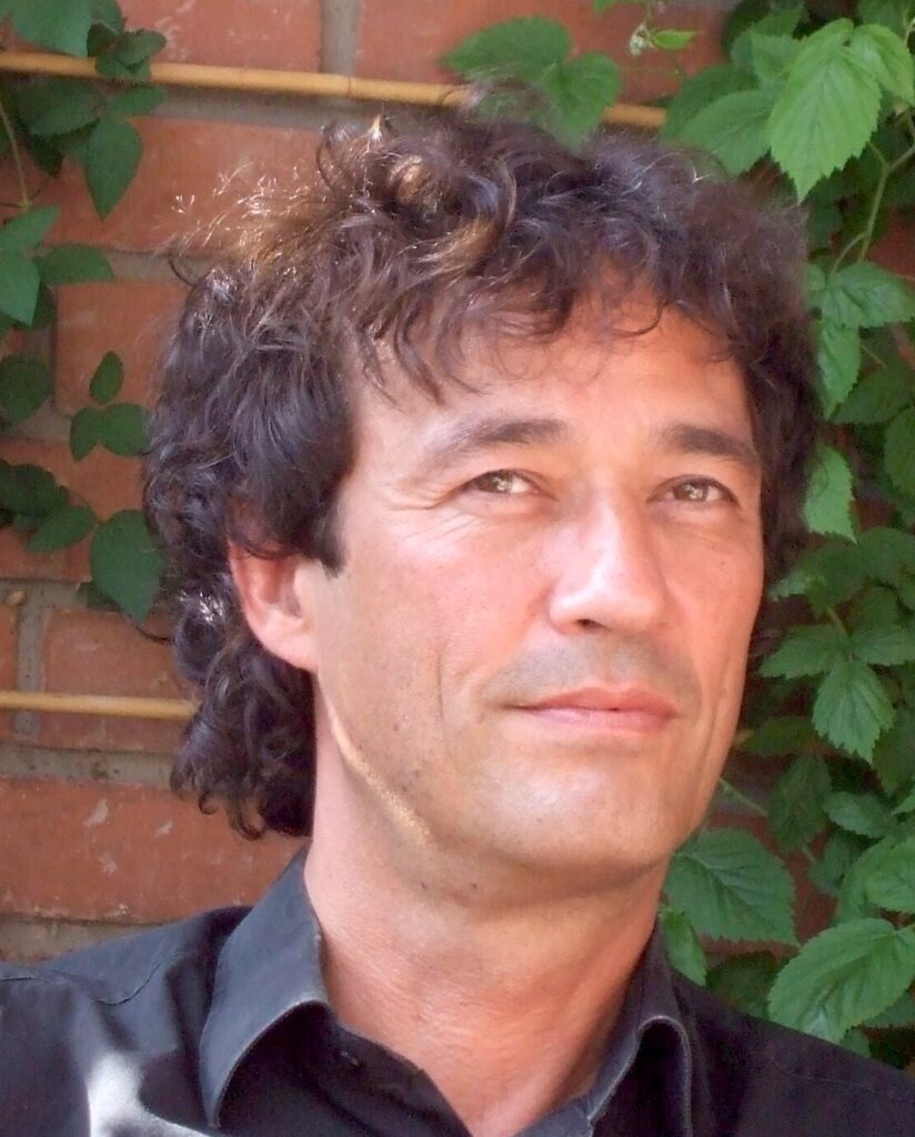 Portrait photo of Werner standing against a brick wall with leaves