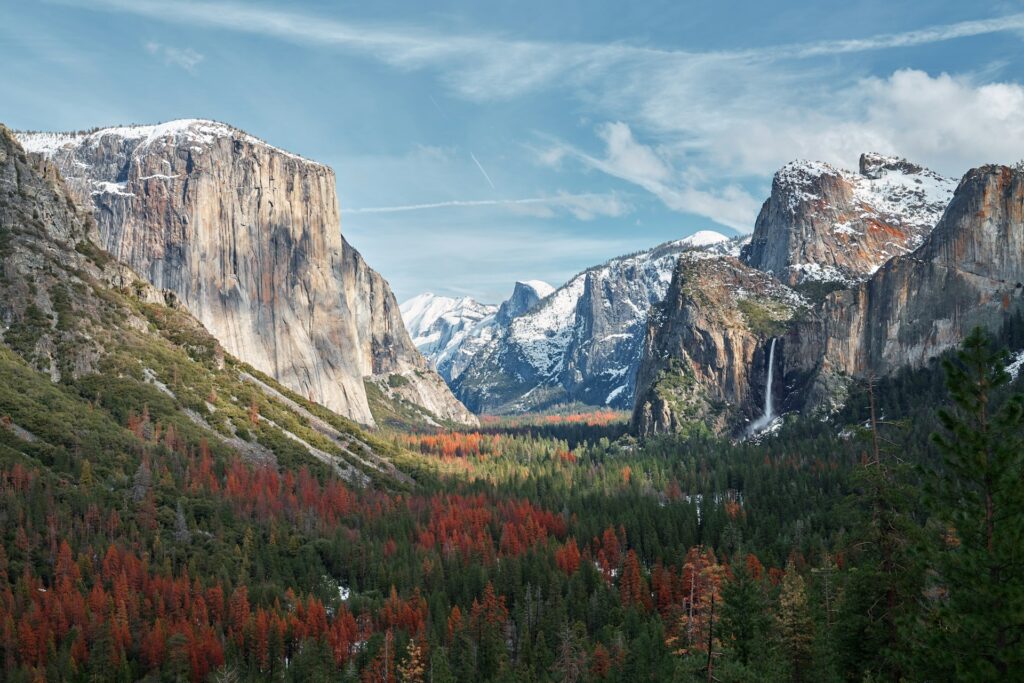 Image of Yosemite Valley in the late fall, with snow-capped mountains, orange-tinged tree line and blue skies