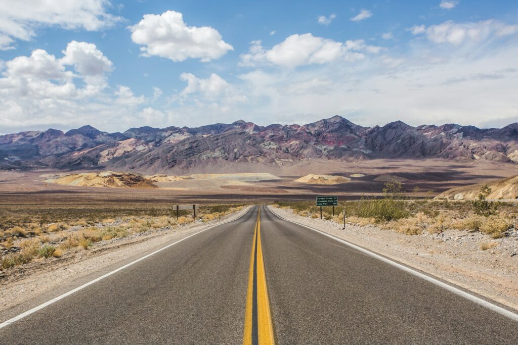 Photo taken looking down a highway towards a desert landscape in Death Valley National Park