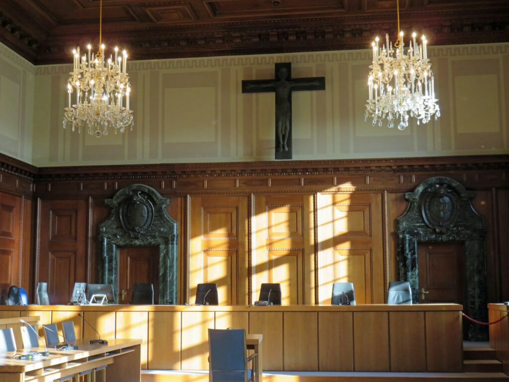 A photo of Courtroom 600 in Nuremberg, featuring a large crucifix placed on the far wall and hanging candelabra-style lights