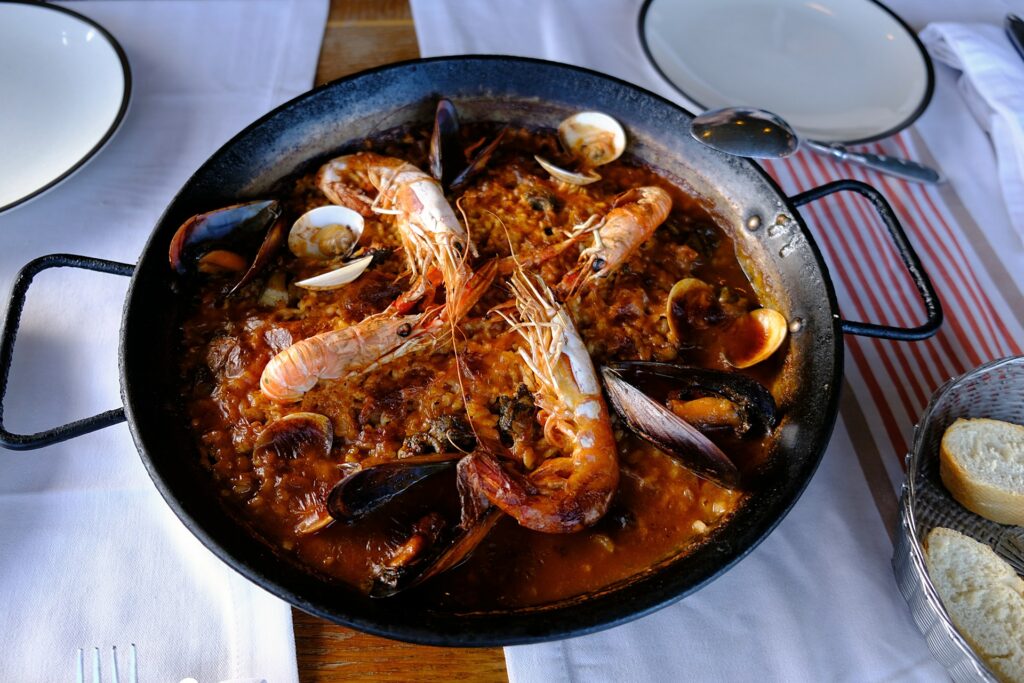Photo of a steel paella pan containing prawn paella, on a table with a red and white table cloth