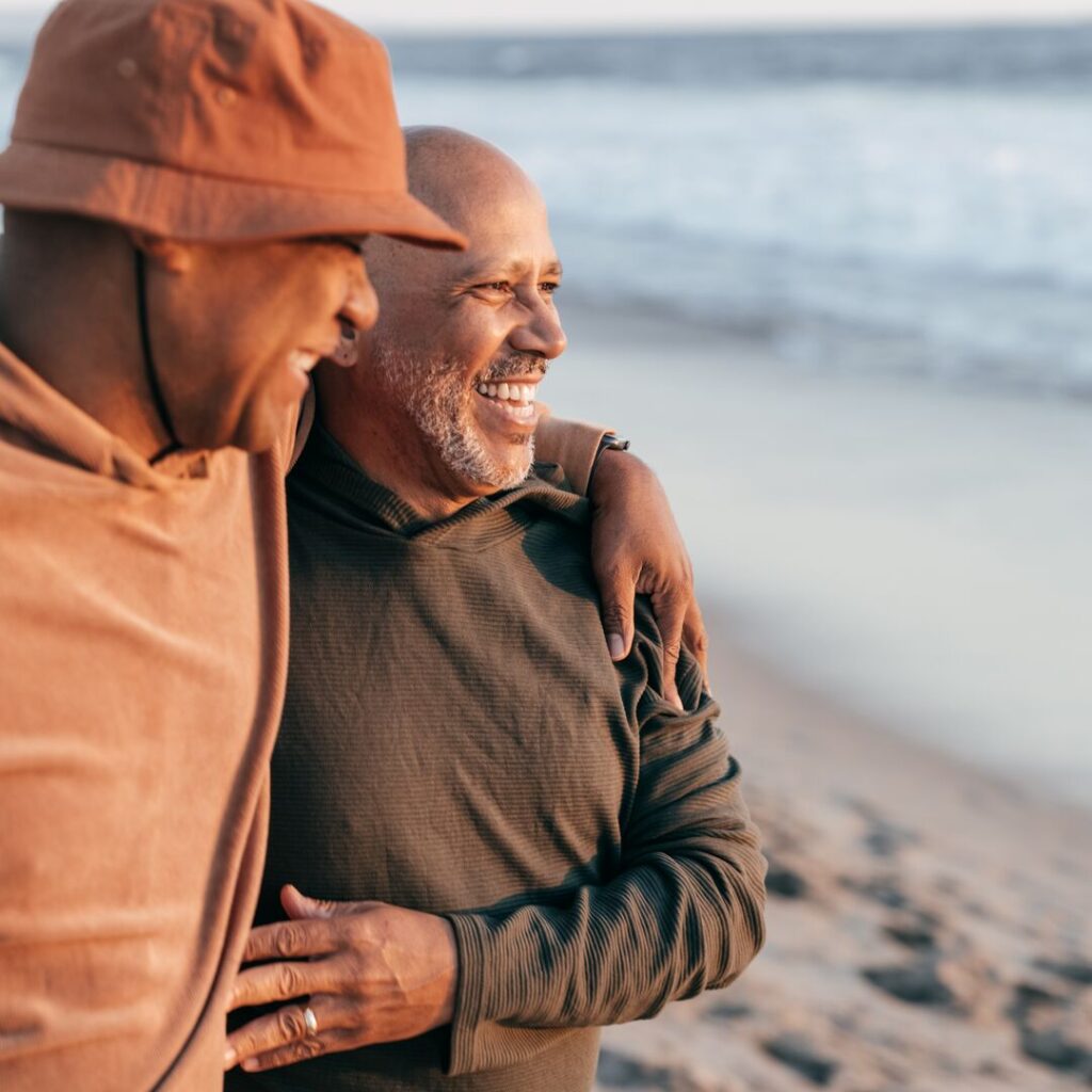 Two men laughing while arm-in-arm, walking along a beach