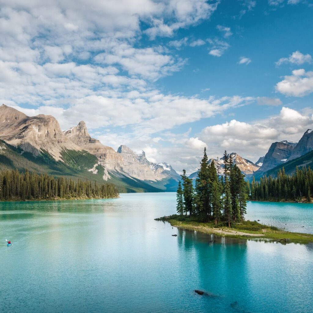 A glassy lake in Canada, reflecting the blue sky and a tumbling mountain range in the background