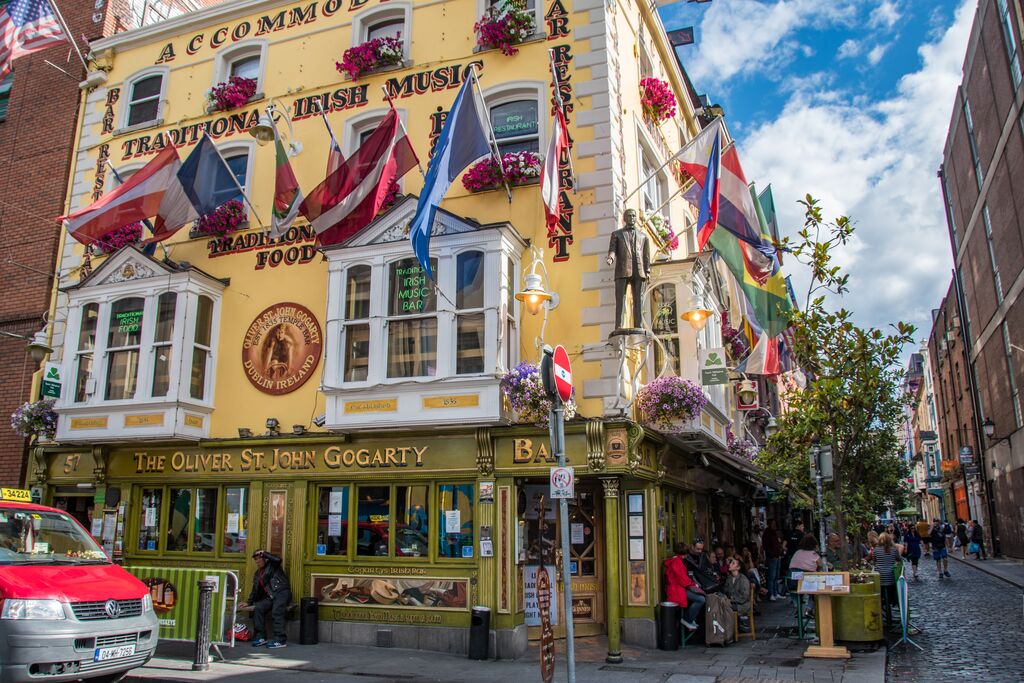 The colorful front facade of an Irish pub, lined with waving flags and colorful wreaths below the windows.