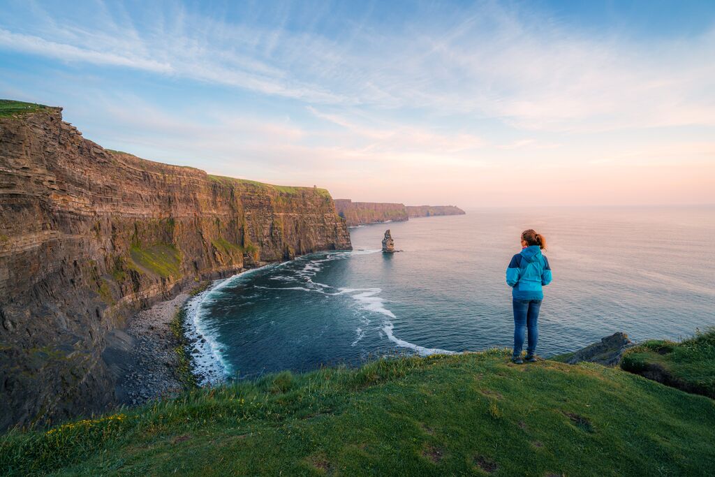 Woman looking into the distance over the sea and cliffs as the sun sets in Ireland in May