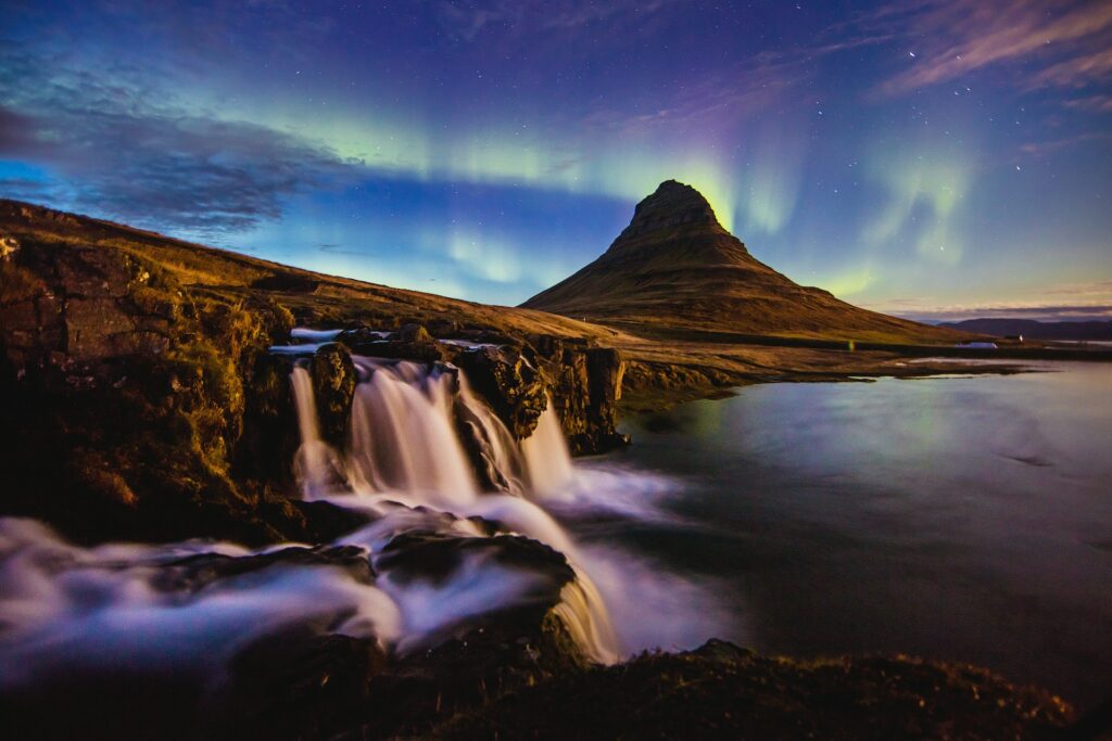 Northern Lights photographed in the night sky over a conical volcano and waterfall in Iceland