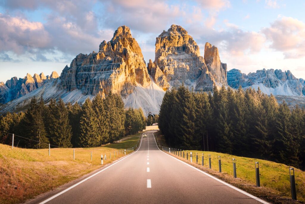A long straight road leans into the Dolomite mountains in Italy.