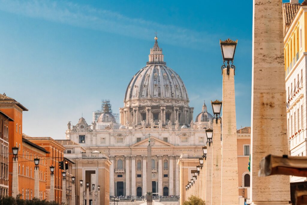 The street to St Peter’s Basilica in Rome, lined with other ancient buildings is shown against a blue sky