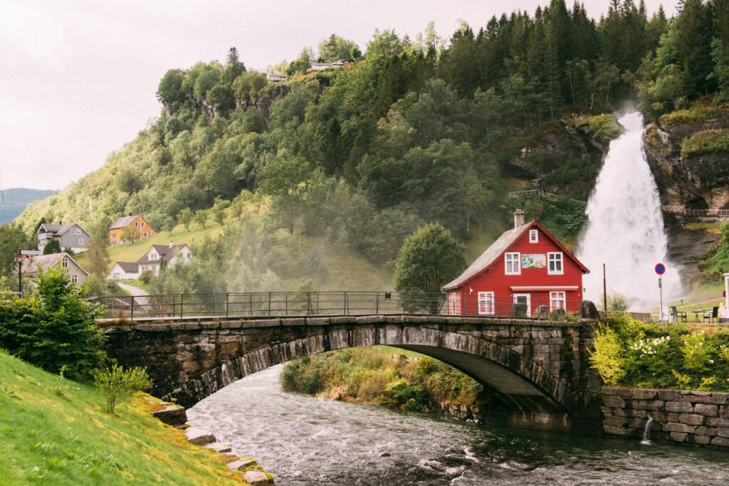 Typical red cottage in an idyllic Scandinavia landscape with a waterfall and bridge over a river